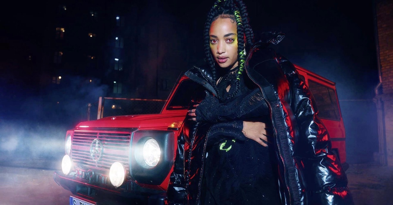 Artist in dark fashion beside a red vehicle at night